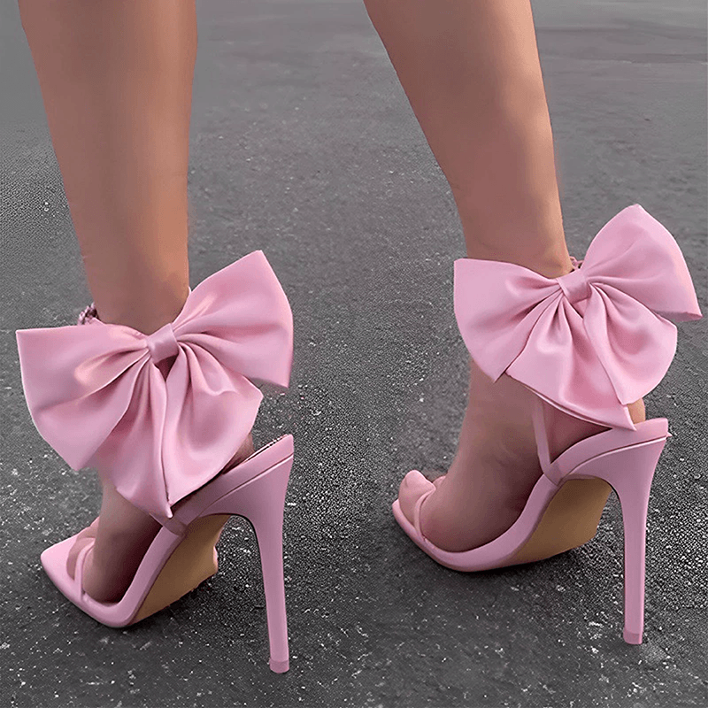Pink ankle strap stiletto sandals worn from rear with bows visible